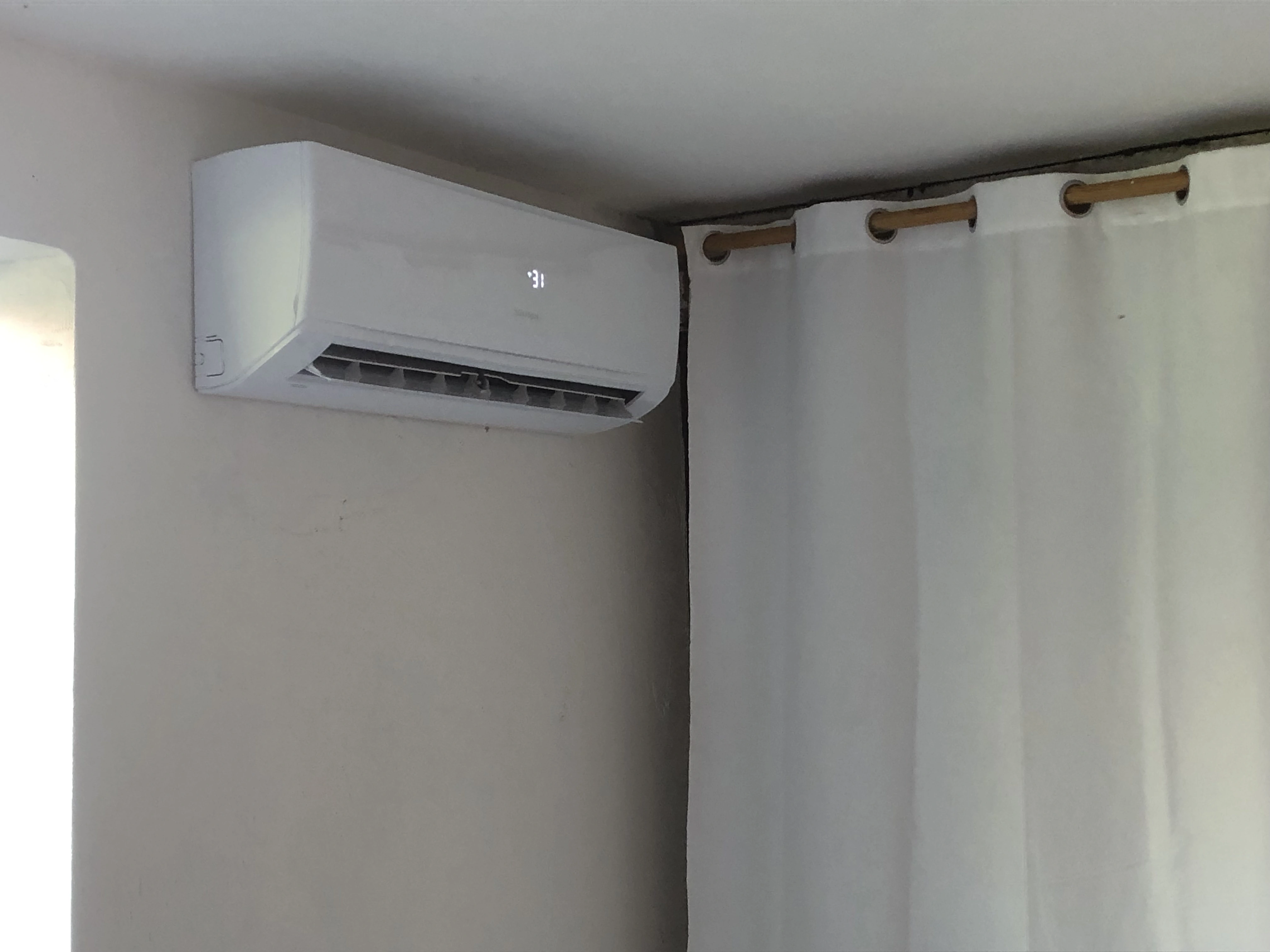 Vnútorná jednotka klimatizácie v rohu miestnosti pri okne na stene