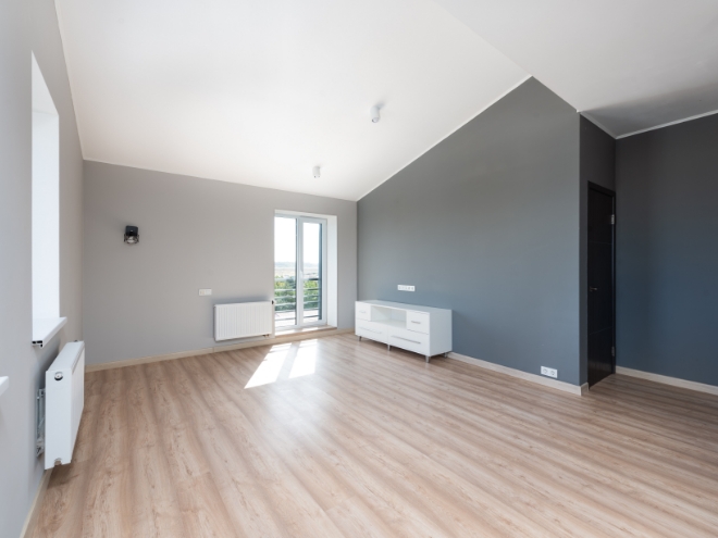 Prázdna miestnosť s šedými stenami, radiatormi a drevenými podlahami.